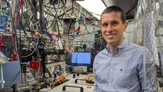 A man in a collared shirt stands in front of lab equipment and many hanging cables.