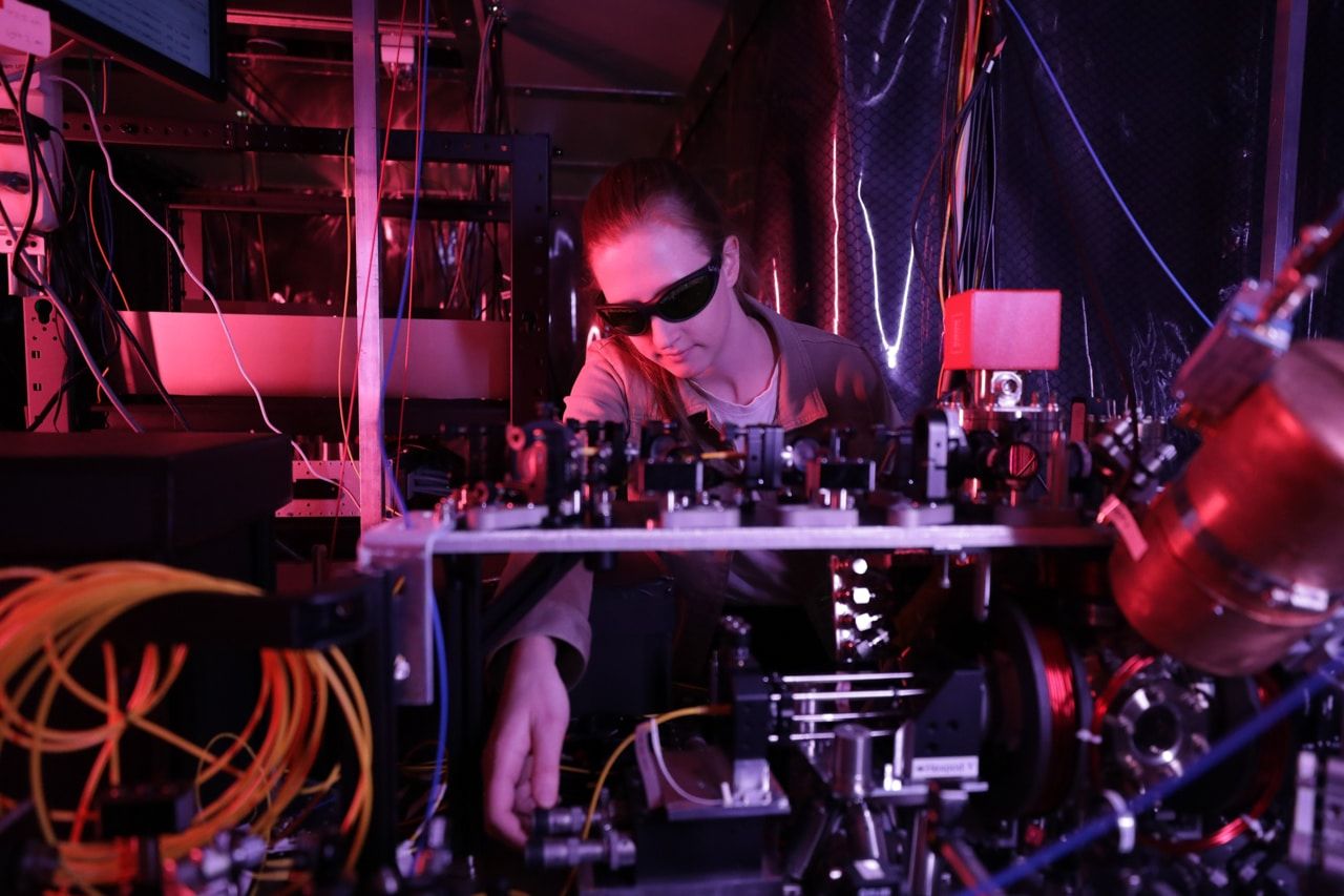 A woman with sunglasses works on electronic equipment surrounded by wires