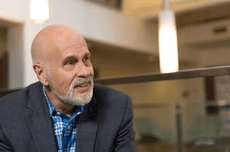 Robert Calderbank wearing a grey blazer and blue checkered shirt, pictured in a modern office environment with a blurred background.
